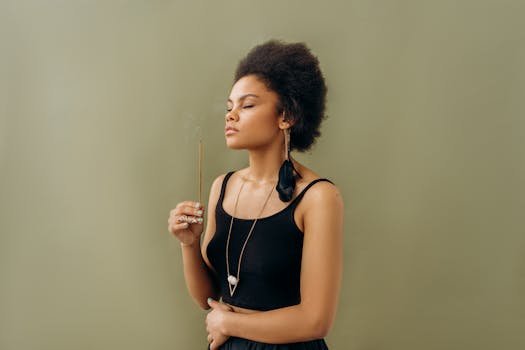 Serene young woman practicing aromatherapy with incense stick indoors, promoting wellness.